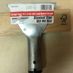 May include: A straight back wire brush with a large beveled scraper. The tool has a wooden block and a stainless steel head and handle. The text on the label reads "Stainless Steel Will Not Rust".