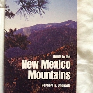 Puede incluir: Una portada de libro con una foto de una cordillera montañosa y un pino. El título es "Guide to the New Mexico Mountains" de Herbert E. Ungnade.