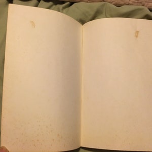 Puede incluir: Un libro blanco abierto con p&aacute;ginas blancas. Las p&aacute;ginas est&aacute;n ligeramente amarillentas y tienen algunas peque&ntilde;as manchas marrones.