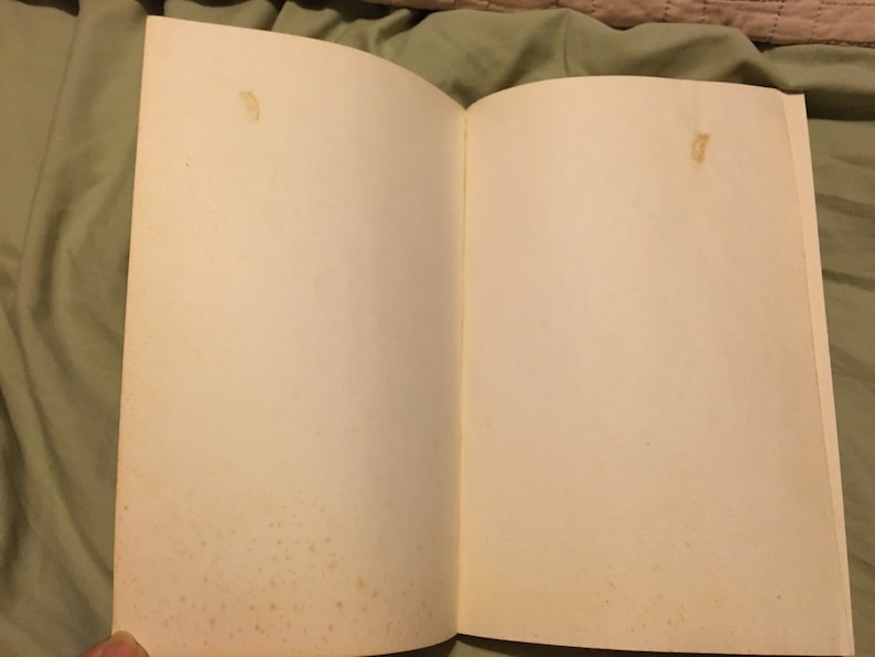 Puede incluir: Un libro blanco abierto con p&aacute;ginas blancas. Las p&aacute;ginas est&aacute;n ligeramente amarillentas y tienen algunas peque&ntilde;as manchas marrones.