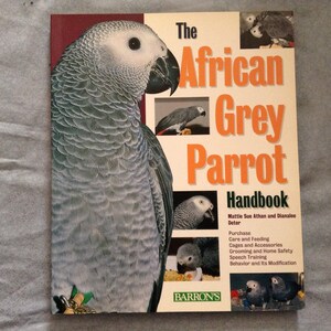 May include: A book titled "The African Grey Parrot Handbook" by Mattie Sue Athan and Dianalee Deter. The cover features a close-up of a grey parrot and several smaller images of parrots.