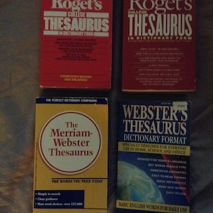 May include: Four different thesaurus books with red, yellow, and blue covers. The books are titled "Roget's College Thesaurus", "Webster's Thesaurus", and "The Merriam-Webster Thesaurus".