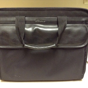 May include: Black leather laptop bag with a handle and a zipper closure. The bag has a brand name "Targus" printed on the front.