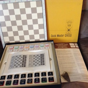 May include: A vintage Quick Master Chess game set. The set includes a checkered game board, chess pieces, and a yellow box with the game's title. The pieces are black and white with colorful accents.