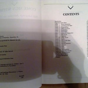 May include: A book titled "Come Sign With Us" with a white cover and black text. The book is a guide to sign language activities for children. The book includes a table of contents with a list of lessons, including facial expressions, learning to see signs, finger spelling, asking questions, saying hello, name signs, classroom cooperation, the family, opposites, action words, sports, days of the week, holidays, signing sentences, animals, food, colors, transportation, make new friends, communication, creative use of signing, annotated bibliography, and glossary.