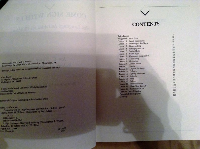May include: A book titled "Come Sign With Us" with a white cover and black text. The book is a guide to sign language activities for children. The book includes a table of contents with a list of lessons, including facial expressions, learning to see signs, finger spelling, asking questions, saying hello, name signs, classroom cooperation, the family, opposites, action words, sports, days of the week, holidays, signing sentences, animals, food, colors, transportation, make new friends, communication, creative use of signing, annotated bibliography, and glossary.