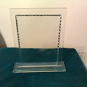 May include: A clear glass picture frame with a decorative beaded border. The frame is standing on a green surface.