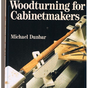 May include: A book titled "Woodturning for Cabinetmakers" by Michael Dunbar. The cover features a close-up of a woodturning lathe with a piece of wood being turned.