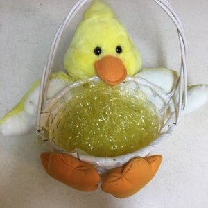 May include: A yellow plush chick Easter basket with a white wicker base and orange feet. The basket is filled with yellow shredded paper.