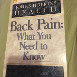 Puede incluir: Una portada de libro con fondo blanco y texto azul y negro. El t&iacute;tulo es "Back Pain: What You Need to Know" y el subt&iacute;tulo es "Johns Hopkins Health".