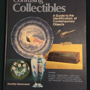 Op de afbeelding: Boekomslag met de titel "Confusing Collectibles: A Guide to the Identification of Contemporary Objects" door Dorothy Hammond. De omslag toont een selectie van kleurrijke objecten, waaronder een blauw-witte vaas, een groen-witte glazen bol en een houten vogel.