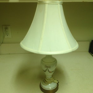 May include: A white porcelain table lamp with a floral design and a white lampshade. The lamp has a gold base.