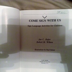 May include: A book titled "Come Sign With Us: Sign Language Activities for Children" by Jan C. Hajer and Robert M. Wilson. The book cover features a diamond shape and the title in black text.