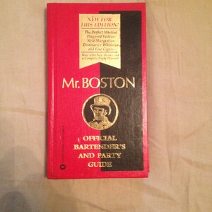 May include: A red and black book titled "Mr. Boston Official Bartender's and Party Guide". The cover features a gold banner with the text "New for this Edition!" and a black and white illustration of a man in a hat.