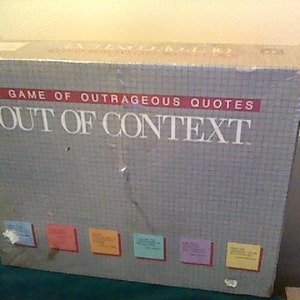 May include: A game box for a game called "Out of Context", a game of outrageous quotes. The box is silver with a grid pattern and the title is in red and white.