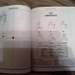 May include: A black and white illustrated book page with the title "Lesson 9: Opposites". The page features a series of illustrations of people signing words in American Sign Language. The words include "I", "What", "Do", "You", "Know", "About", and "Opposites?"
