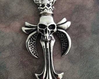 May include: A silver pendant necklace featuring a skull with a crown on top, set within a stylized fleur-de-lis design.