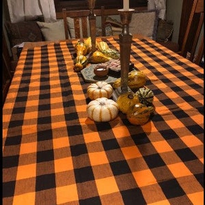 A black and orange checkered tablecloth with gourds and small pumpkins on top. The tablecloth is set on a wooden table with candlesticks and candles.