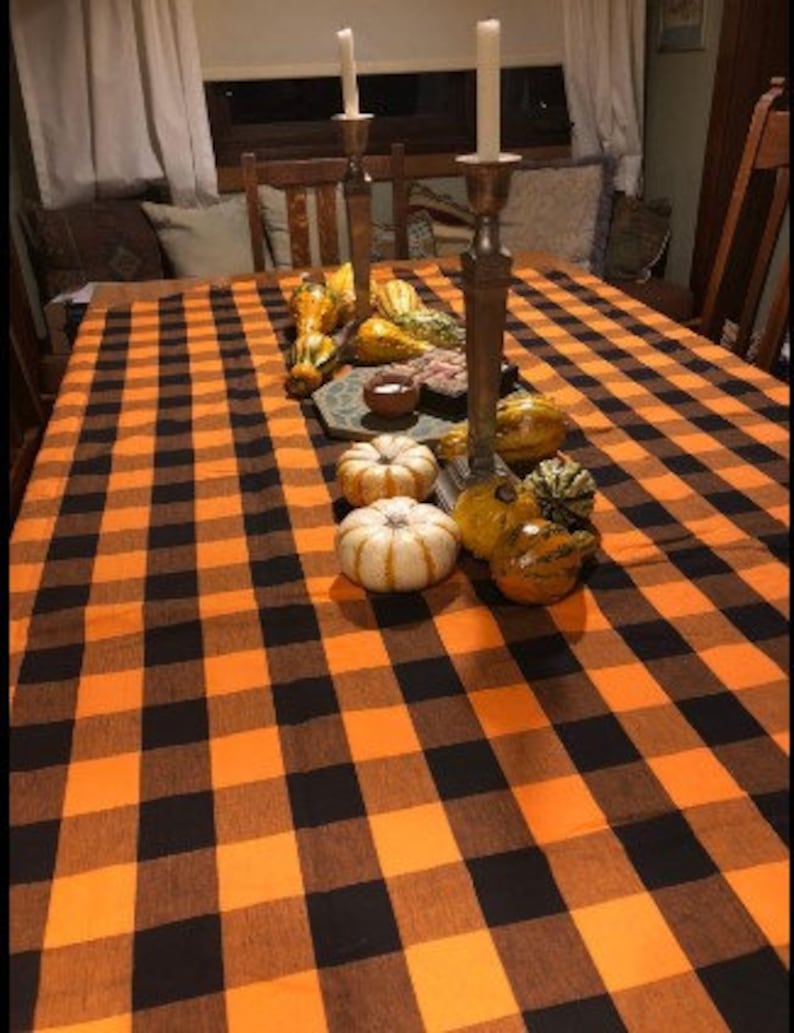 A black and orange checkered tablecloth with gourds and small pumpkins on top. The tablecloth is set on a wooden table with candlesticks and candles.