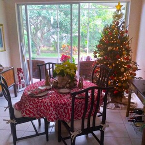 A dining room set for a holiday celebration. A round table is set with a red and white Japanese tablecloth, plates, and napkins. Black chairs surround the table. A decorated Christmas tree with lights and ornaments stands in the corner.