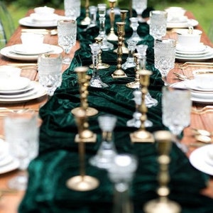 A long table setting with a green velvet runner and gold candle holders. The table is set with white plates, clear glasses, and gold silverware.