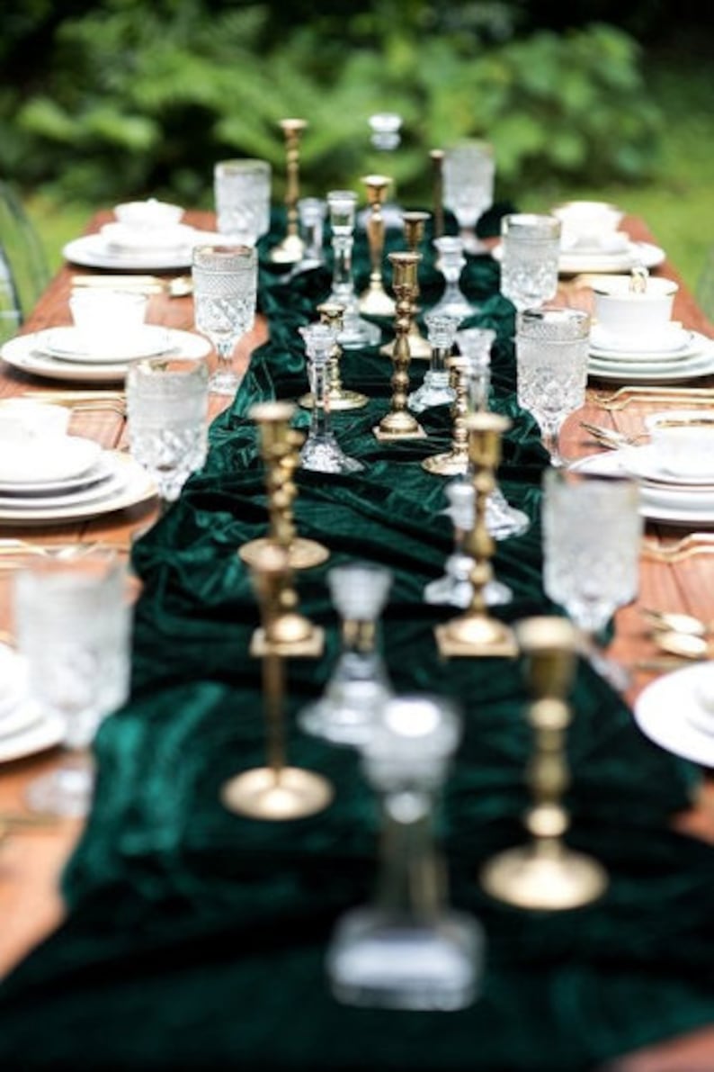 A long table setting with a green velvet runner and gold candle holders. The table is set with white plates, clear glasses, and gold silverware.