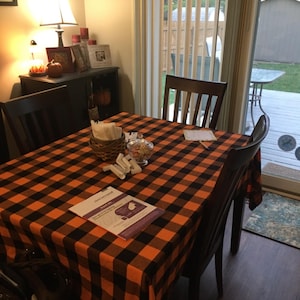 A  table setting with a black and orange checkered tablecloth. This fabric is also called buffalo plaid tablecloth and is manufactured by Premier Linens.