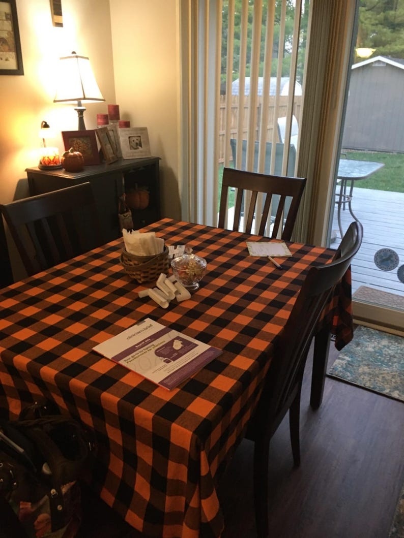 A  table setting with a black and orange checkered tablecloth. This fabric is also called buffalo plaid tablecloth and is manufactured by Premier Linens.