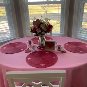 pink tablecloth and red placemats on a romantic table setting. It is a small table in a home overlooking the front yard.