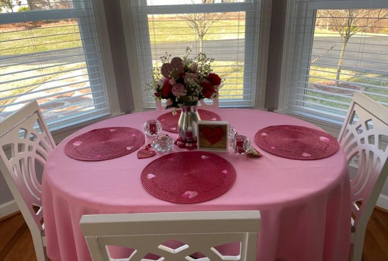 pink tablecloth and red placemats on a romantic table setting. It is a small table in a home overlooking the front yard.
