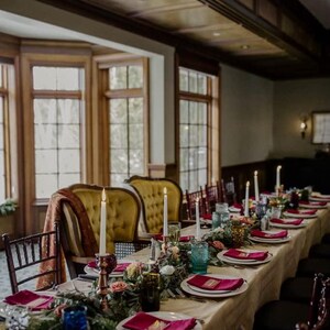 A long wedding reception table with a tan tablecloth and red linen napkins ready for the wedding reception dinner.