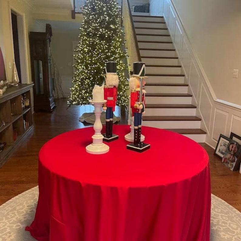 Red Christmas tablecloth in a home during the holidays with a Christmas tree in the hallway. It is a plush velvet tablecloth that looks stunning.