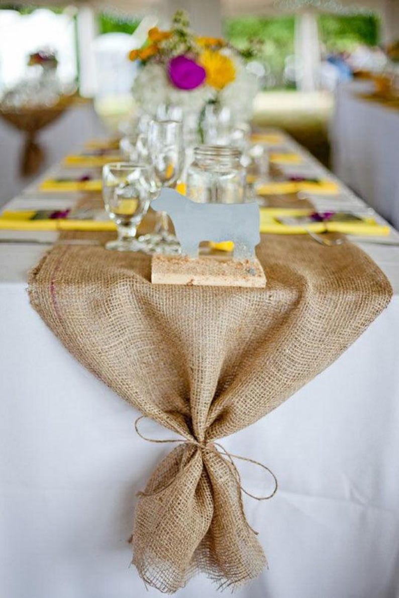 a wedding reception with a long burlap table runner. The end of the burlap runner is tied off with jute rope.