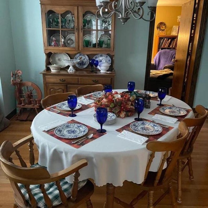 White tablecloth, napkins and placemats as well as china and glass on a custom size oval table set for an elegant meal.