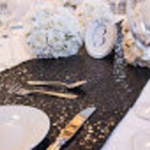 May include: Black table runner with silver glitter, white plates, silverware, and white decorative balls.