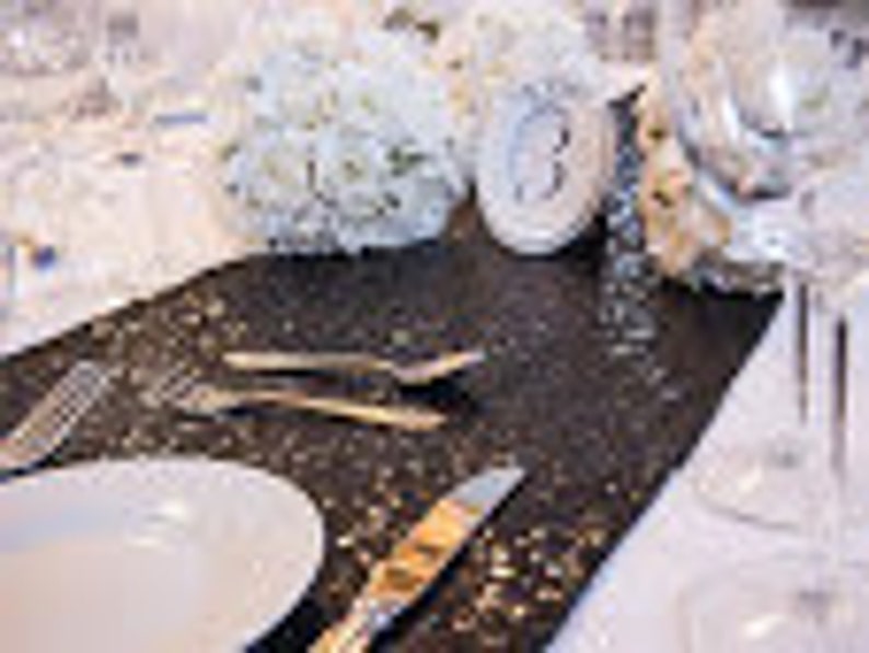 May include: Black table runner with silver glitter, white plates, silverware, and white decorative balls.