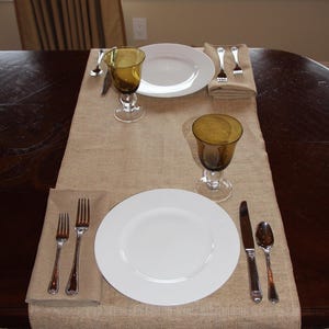 A table with a burlap table runner set for a meal for two.