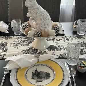 A formal table set for an Easter celebration with fine china and cotton napkins. There is a large Easter bunny sculpture on the table and eggs.