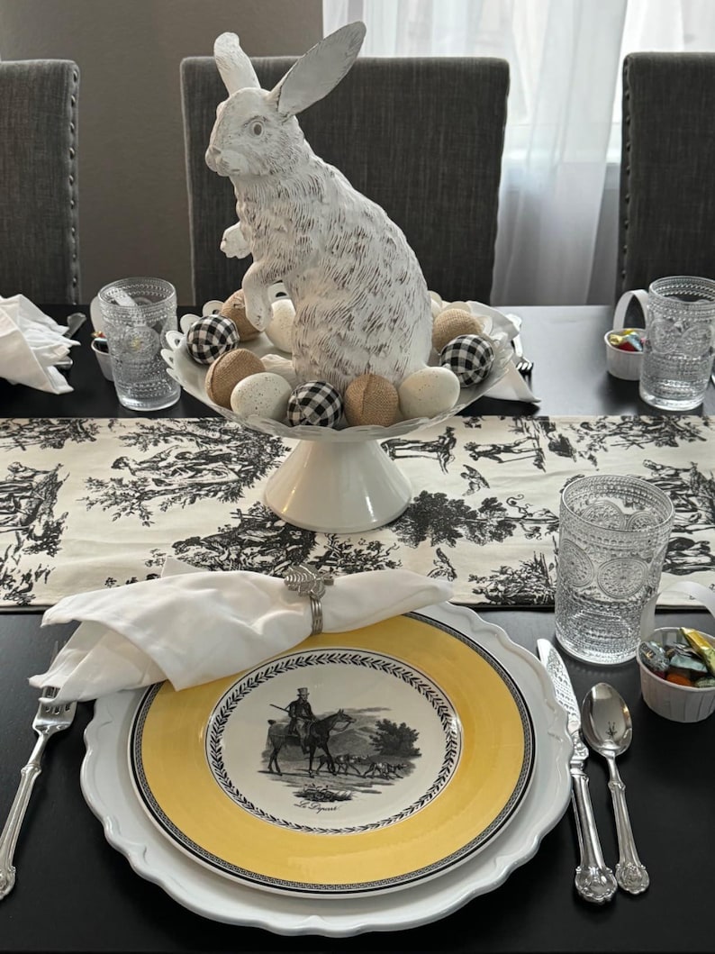 A formal table set for an Easter celebration with fine china and cotton napkins. There is a large Easter bunny sculpture on the table and eggs.
