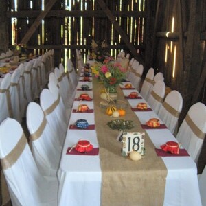 A long table with white linens and burlap runners is set for a wedding reception. The table is decorated with flowers and has place cards with the number 18 on them.
