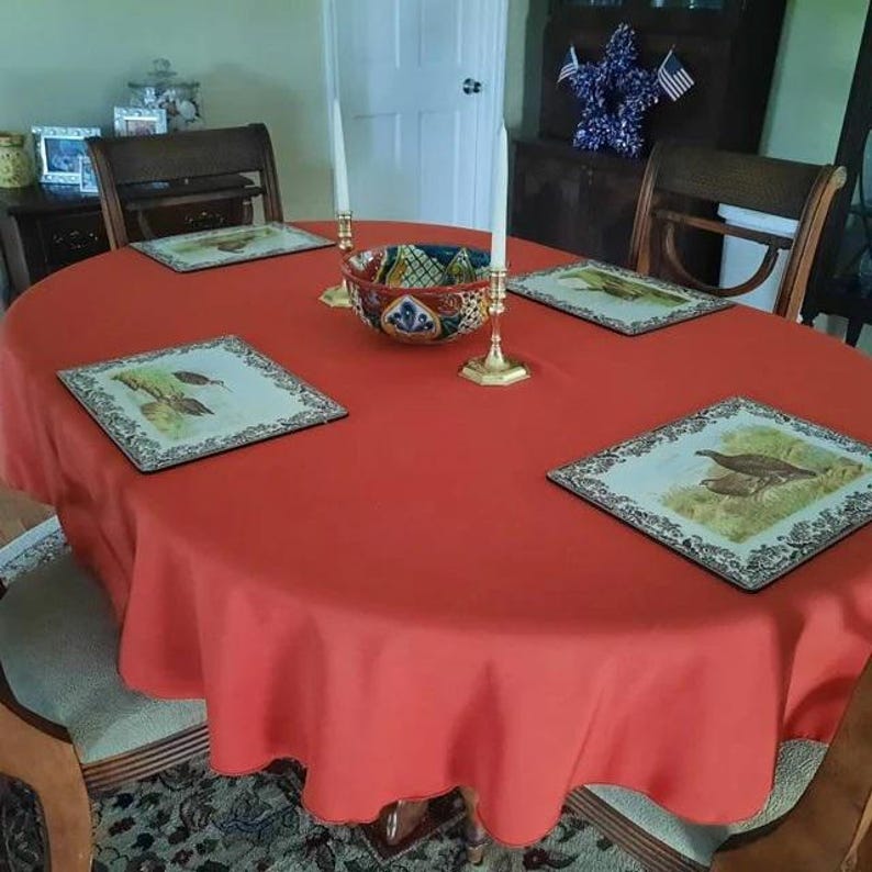 oval burnt orange tablecloth farmhouse dining room dinner table. Tablescape is decorated for autum. The tablecloth is a nice polyester tablecloth.