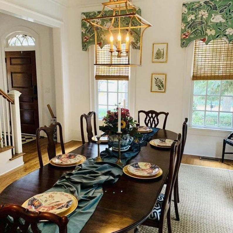 A green velvet table runner drapes over a wooden table set for a dinner party in a home.