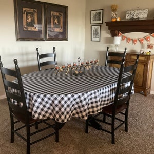 May include: A black and white checkered tablecloth covers a round table with six black chairs. The table is set with a candelabra and candles. The room has a farmhouse style with a wooden mantle and a welcome sign.