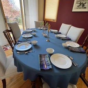 Large blue oval tablecloth and napkins with china and candles on the large custom size table.
