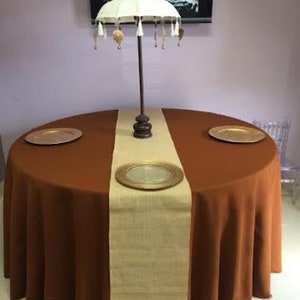 A brown round tablecloth with a burlap table runner and two gold chargers. A white umbrella with gold tassels is in the center of the table.