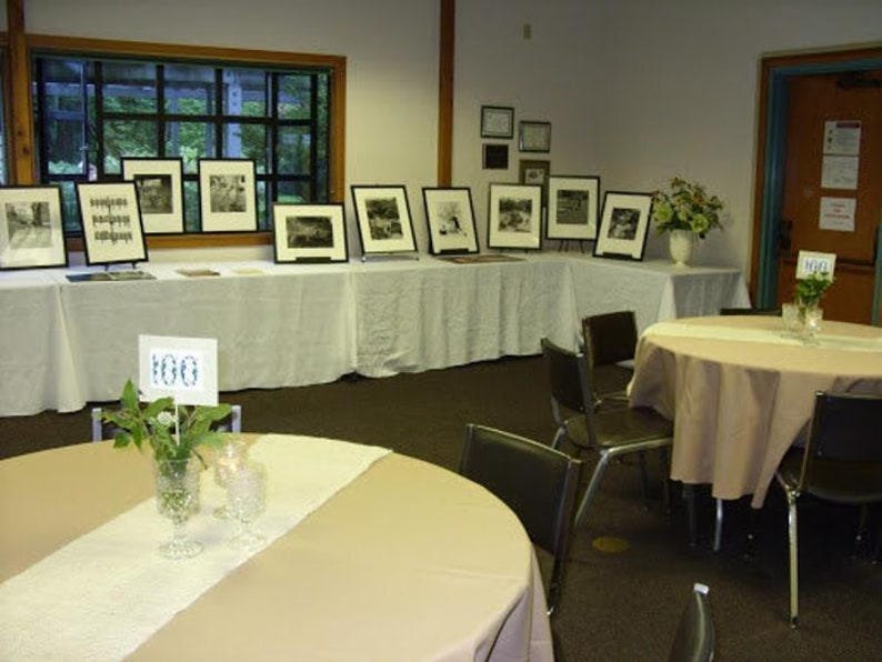 A paint exhibit. Over the tablecloths are white burlap table runners.