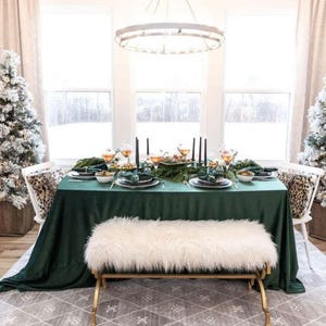 Green velvet tablecloth set on a rectangular table with fine china, floral arrangements and candles at a wedding reception. Through the window in the room we see a lot of snow outside.