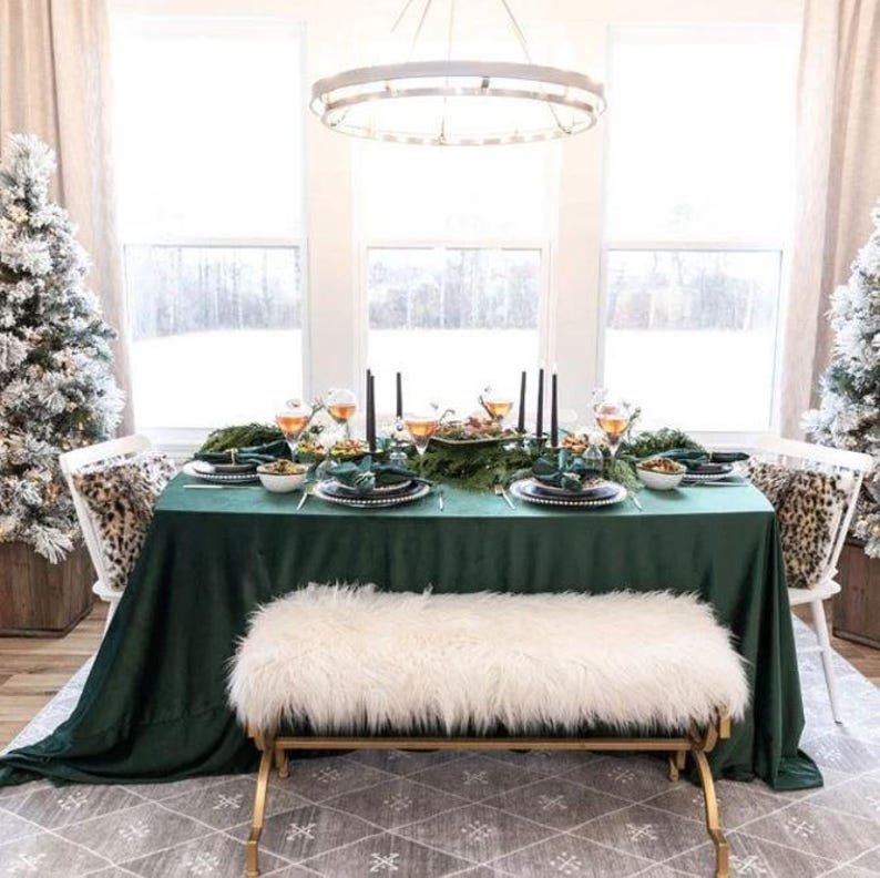 Green velvet tablecloth set on a rectangular table with fine china, floral arrangements and candles at a wedding reception. Through the window in the room we see a lot of snow outside.