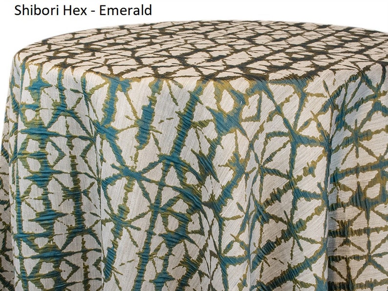 Moss green Shibori tablecloth with a geometric Shibori Hex pattern. The fabric has a textured appearance with a repeating diamond and line design. The tablecloth is draped over a round surface. The tablecloth manufacturer is Premier Linens.