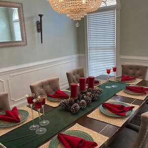 May include: A dark wood dining table set for a holiday dinner with green placemats, red napkins, and gold-rimmed plates.  There are red candles and pine cones in the center of the table.